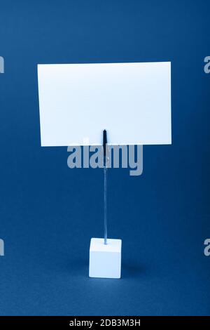 Leere weiße Pappe mit Kopie Speicherplatz auf klassischen Metal Hinweis Inhaber über Dunkelblau Papier Hintergrund, Vorderansicht Stockfoto