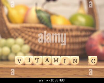 Kleine Holzblöcke mit den Worten Vitamin C auf einem Küchentisch mit frischen Früchten im Hintergrund, gesundes Lebensmittelkonzept Stockfoto