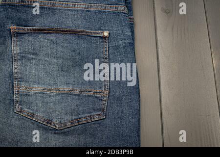Rückentasche einer gewaschenen blauen Denimhose mit Goldnähten auf grauem Holzhintergrund Stockfoto