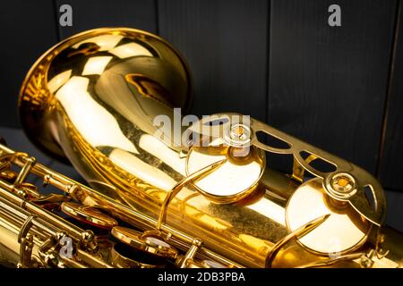 Die Glocke und einige Noten Tasten eines Tenorsaxophons im Vordergrund auf grauem Holzhintergrund Stockfoto