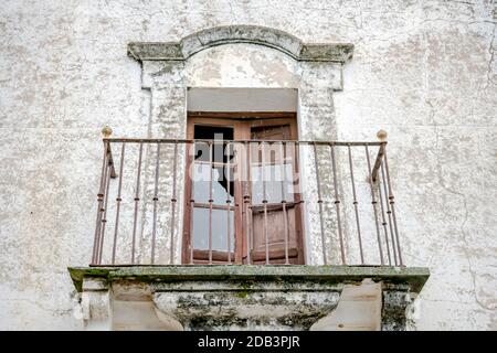 Fenster mit Zugang zu altem Balkon und schmiedeeisernem Zaun, das im Laufe der Zeit an einer Fassade eines alten und rustikalen Hauses schmiedet wurde Stockfoto