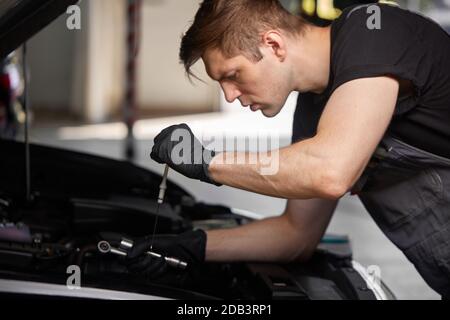 Junge kaukasische professionelle Auto-Mechaniker in einem Auto-Service, prüft ein Auto, Motor, Vergaser. Auto-Reparatur, Fehlerdiagnose, Reparatur-Spezialist, Wartungskonzept Stockfoto