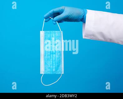 Sterile Handschuhe aus blauem Latex halten eine blaue Einwegmaske aus Vliesstoff auf blauem Grund, Schutzzubehör für die Atemschutzmaske Stockfoto