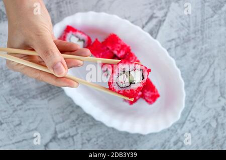 Japanisches Sushi-Essen. Weibliche Hand hält Sushi. Draufsicht auf Sushi auf weißem Teller. Speicherplatz kopieren. Weichfokus Stockfoto