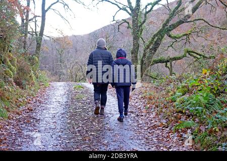 Rückansicht des Jungen 10 oder 11 auf dem Weg Spaziergang mit der Mutter im Herbst an kalten nassen Tagen Entlang der Landstraße Carmarthenshire Wales Großbritannien KATHY DEWITT Stockfoto