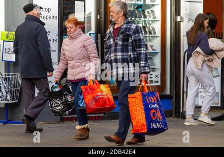 Dundee, Tayside, Schottland, Großbritannien. November 2020. UK News Covid-19 Lockdown. Menschen, die in Dundee auf den Straßen herumlaufen und nur wenige wichtige Bekleidungsgeschäfte geöffnet haben, da die strengere Stufe 3 Covid-19 Lockdown-Beschränkung durchgesetzt wurde. Ein Paar kennt die sozialen Distanzierungsrichtlinien und das Tragen von Gesichtsmasken, die an einem kalten und sonnigen Novembernachmittag zusammen mit großen Marken-Tragetaschen bei ihren frühen Weihnachtseinkäufen im Stadtzentrum herumlaufen. Kredit: Dundee Photographics/Alamy Live Nachrichten Stockfoto