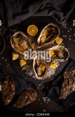 Austern serviert auf schwarzem Schieferbrett mit Eis und Zitrone Stockfoto