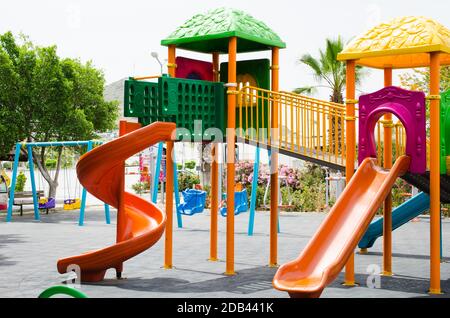 Bunte Aktivitäten auf dem Spielplatz im öffentlichen Park, umgeben von grünen Bäumen. Spielplatz ohne Kinder Stockfoto