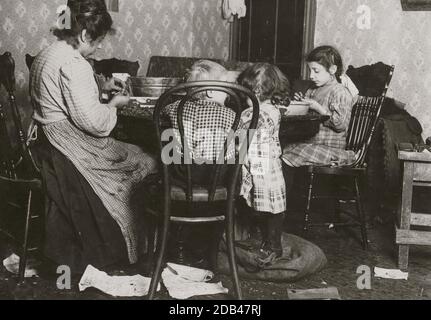 Frau Lucy Libertine und Familie: Johnnie, 4 Jahre alt; Mary, 6 Jahre; Millie, 9 [?] Jahre, Kommissionierung Nüsse im Keller Mietshaus, 143 Hudson St. Mary stand in der offenen Öffnung der Tasche mit den gerissenen Nüsse (gepflückt werden), mit ihren schmutzigen Straßenschuhe an, und mit einem riesigen schmutzigen Jackmesser. Auf der rechten Seite ist die Bank des Schusters in diesem Raum verwendet. Sie leben in dunklen Innenzimmern, und Schmutz ist im ganzen Zimmer und im dunklen, feuchten Eingang reichlich vorhanden. Stockfoto