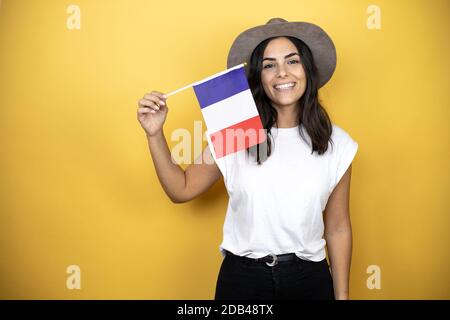 Schöne Frau trägt lässiges weißes T-Shirt und einen Hut stehen Auf gelbem Hintergrund mit der französischen Flagge Stockfoto