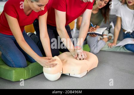 Junger Mann übt CPR erste Hilfe an einer Schaufensterpuppe in Anwesenheit von Menschen, drinnen Stockfoto