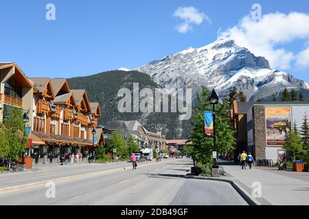 Banff Avenue, die zentrale Straße der Innenstadt von Banff in Kanada an einem sonnigen Tag. Kanadische Touristenstadt mit dem Mount Norquay dahinter. Stockfoto