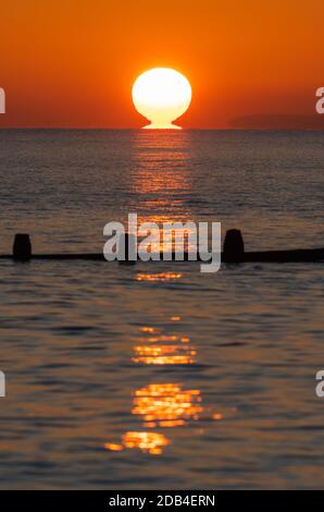 Porträt eines tiefen Sonnenuntergangs über dem Meer. Vertikal des Sonnenuntergangs über dem Meer mit Sonne, die das Wasser berührt. Stockfoto