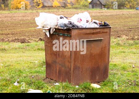 Überfließender rostiger Mülleimer auf dem Land. Müll auf dem Boden verstreut, Umweltschutz Problem Stockfoto