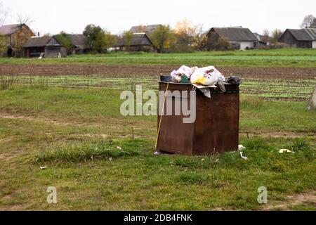 Überfließender rostiger Mülleimer auf dem Land. Müll auf dem Boden verstreut, Umweltschutz Problem Stockfoto