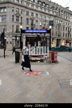 Eine Frau, die eine schützende Gesichtsmaske trägt, geht an einem NHS-Hinweisschild vor der U-Bahnstation Oxford Circus vorbei, während die zweite nationale Sperre in England greift. Stockfoto