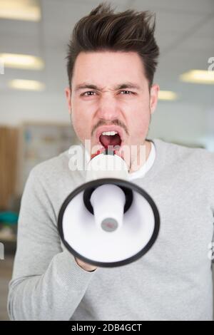 Portrait des jungen Mannes stattlich schreiend mit Megaphon innen Stockfoto