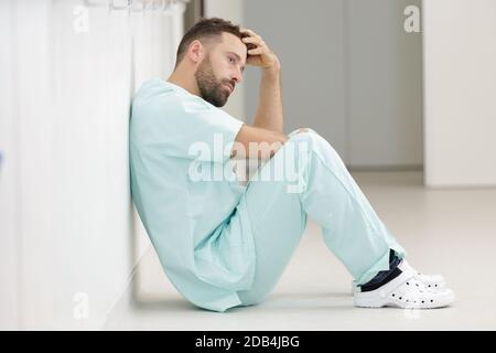 Trauriger Chirurg, der auf dem Boden im Flur im Krankenhaus sitzt Stockfoto