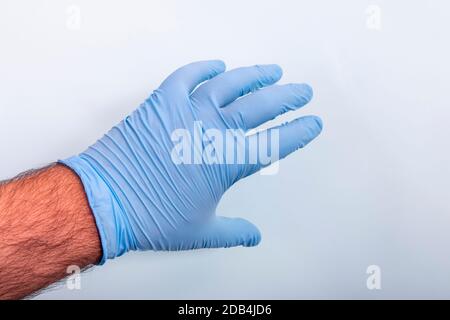 Hand des Arztes in einem blauen medizinischen Handschuh über hellblauem Hintergrund. Stockfoto