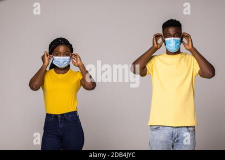 Porträt eines jungen afroamerikanischen Paares mit Schutzmaske während COVID-19, grauer Studiohintergrund. Nahaufnahme von schwarzen Mann und Frau in lov Stockfoto