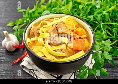 Zentralasiatisches Nationalgericht Lagman von Fleisch, Nudeln und Gemüse in der Schüssel auf einer Serviette, Knoblauch, Petersilie auf Holzbrett Hintergrund Stockfoto