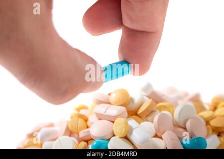 Hand hält eine blaue Pille über einem Haufen anderer verschiedener Pillen. Stockfoto