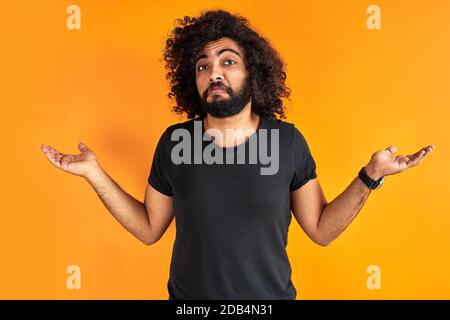 Zweifelhafter arabischer Mann ist Missverständnis, zeigen seine Unverständlichkeit Ausdruck an der Kamera, isoliert über orangenen Hintergrund Stockfoto