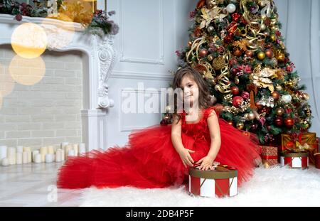 Ein schönes kleines Mädchen in einem luxuriösen Kleid steht in der Nähe Der Weihnachtsbaum Stockfoto