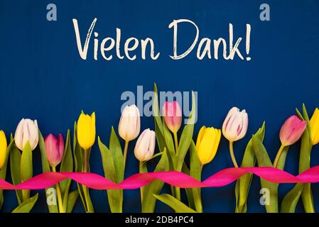 Deutscher Text Vielen Dank Bedeutet Vielen Dank. Weiße Und Pinke Tulpenfrühlingsblumen Mit Band. Blauer Holzhintergrund Stockfoto