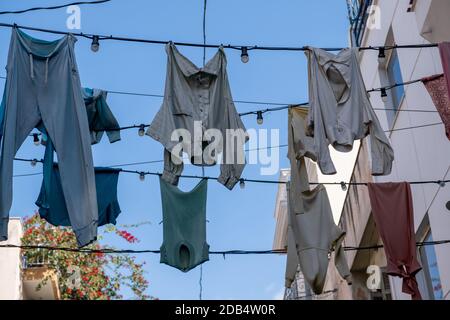 Schäbige Kleidungsstücke hängen und trocknen an elektrischen Kabeln mit Glühbirnen gegen blauen Himmel in der Monastiraki Straße. Athen Griechenland. Tücher natürlichen alten Fashi Stockfoto