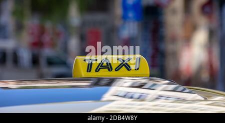 Taxi-Schild auf einem Autodach, gelber und schwarzer Farbtext, Nahansicht, Taxi-Taxi auf der Stadtstraße zur Tageszeit, die auf den Passagier wartet, verwischen das Stadtbild zurück Stockfoto