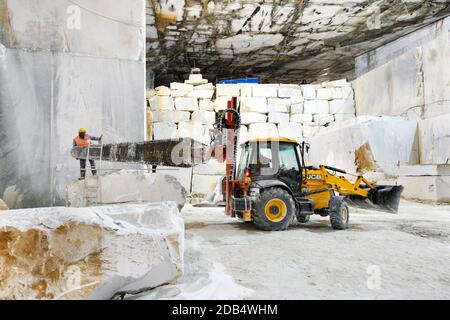 Schneiden von Marmorblöcken in einem Steinbruch oder einer Mine mit einer schweren Diamantsäge, die an der Rückseite eines Frontladers in Carrara, Toskana, Italien befestigt ist Stockfoto