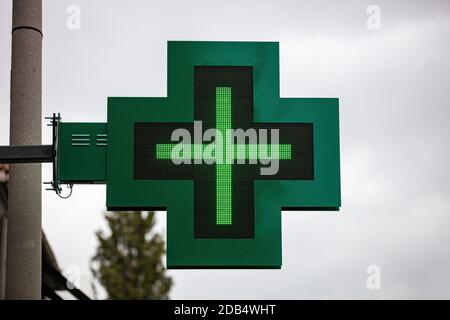 Apothekenzeichen. Grünes Neon Kreuz hängend außerhalb Drogerie Shop gegen bewölkten Himmel in der Stadt Stockfoto