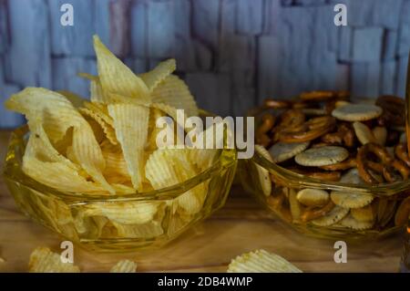 Verschiedene Mischung von salzigen Snacks mit welligen Kartoffelchips, Brezel und Cracker in einer Schüssel und auf einem Holztisch Stockfoto