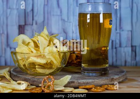 Kaltes Bier und wellige Kartoffelchips in einer Schüssel und Salzige Snacks Brezel auf einem Holztisch Stockfoto