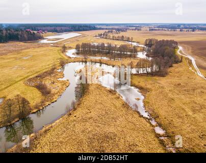 Kleiner Fluss mit trockenen Bäumen ohne Blätter im Winter / Frühfrühling Luftbild. Moody übergossen Wetter. Ackerland, Gärten und Felder in der Region Minsk, Stockfoto
