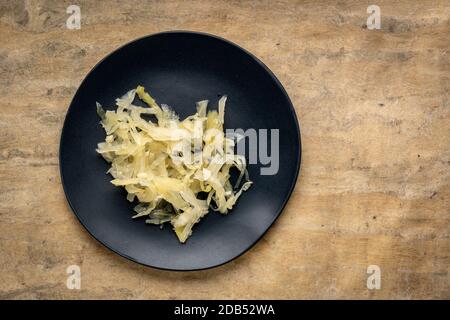 Schwarze Platte mit Sauerkraut vor strukturiertem Papierhintergrund, Probiotikkonzept - fermentierte Lebensmittel gut für die Darmgesundheit Stockfoto