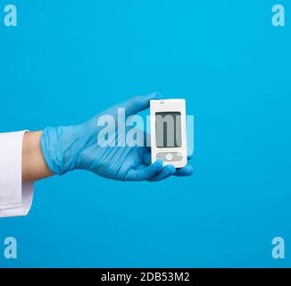 Hand in blau sterile Handschuhe halten ein weißes Blutzucker-Messgerät zur Messung von Blutzuckerwert, blauer Hintergrund Stockfoto