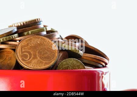 Eingesparte Gelder in einem bunten roten Becher für Finanzziele, die mit Euro-Münzen überlaufen sind, Geschäftskonzept isoliert auf weißem Hintergrund Stockfoto