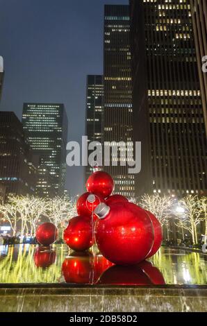 Riesige Weihnachtsschmuck auf einem Brunnen in Manhattan bei Nacht. Große Bälle und helle Lichter Dekoration in 6th Avenue. Wolkenkratzer im Hintergrund Stockfoto