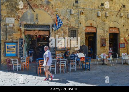 Restaurant im Freien im historischen Zentrum der alten etruskischen Stadt Volterra mit bunten Stühlen und Menschen im Sommer, Pisa, Toskana, Italien Stockfoto