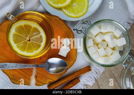 Glas transparente Tasse mit Minztee steht auf einem Holzständer, neben einer Zuckerdose mit Zuckerwürfeln, in Scheiben geschnittene Zitrone und einem Löffel. Stockfoto