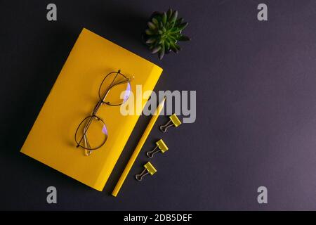 Gelber Bleistift, gelbes Notizbuch und Brille, Stifte, Clip-Papier auf schwarzem Hintergrund. Stockfoto