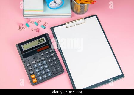 Auf dem rosa Tisch befindet sich ein Taschenrechner und ein Tablet mit einem weißen Blatt, neben gespritztem Wäscheklammern für Papier. Stockfoto