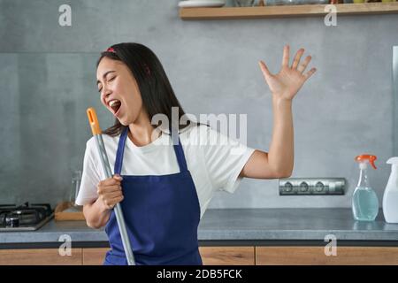 Viel Spaß. Portrait der fröhlichen jungen Frau, Putzfrau vorgibt zu singen, halten Besen während der Reinigung des Bodens, Hausarbeit zu tun. Hausarbeit und Housekeeping Konzept Stockfoto