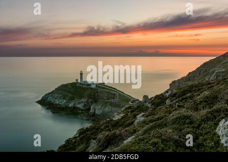 Leuchtturm auf einer Insel an der Küste in Nordwales mit schönem orangefarbenen Sonnenuntergang. Stockfoto
