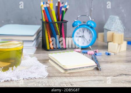 Ein Stapel Bücher, eine Uhr, Holzwürfel in Form einer Pyramide, daneben gibt es Tee mit Zitrone in einem transparenten Glas und bunten Penc Stockfoto