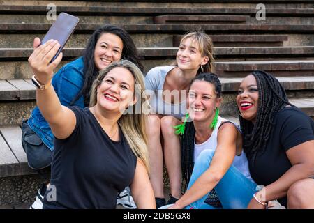 Gruppe von lächelnden jungen Frauen verschiedener Rassen teilen lustige Momente mit dem Smartphone. Konzepte wie Vielfalt, Freundschaft, Gesellschaft Stockfoto