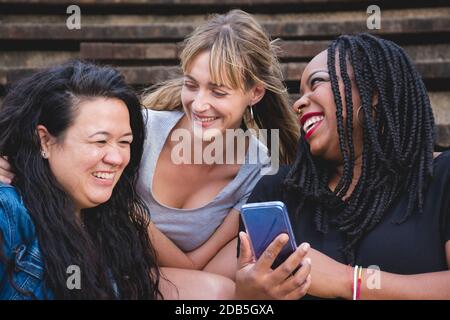 Gruppe von lächelnden jungen Frauen verschiedener Rassen teilen lustige Momente mit dem Smartphone. Konzepte wie Vielfalt, Freundschaft, Gesellschaft Stockfoto