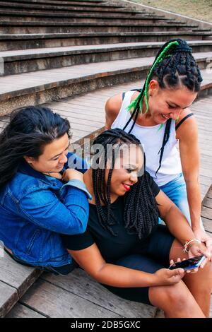 Gruppe von lächelnden jungen Frauen verschiedener Rassen teilen lustige Momente mit dem Smartphone. Konzepte wie Vielfalt, Freundschaft, Gesellschaft Stockfoto